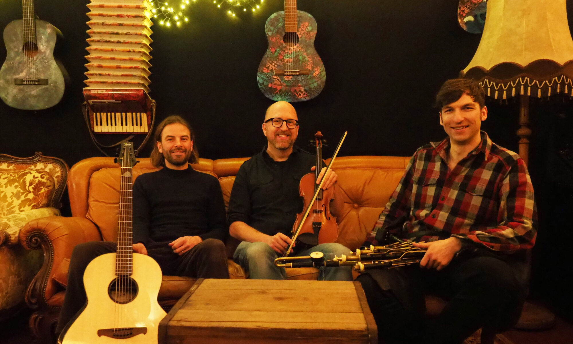 drei irische Musiker sitzen gemütlich auf einer couch mit ihren traditionellen Instrumenten dudelsack, geige und Gitarre dadgad